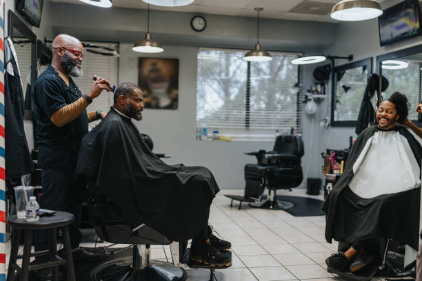 Two black men interact while having their hair trimmed and styled in their neighborhood barber shop.